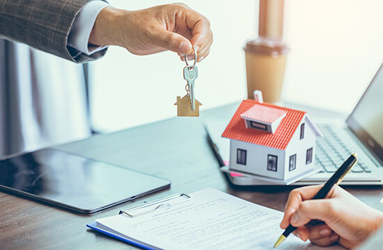 close person handing over the keys to a new home to another person signing mortgage documents at a table.