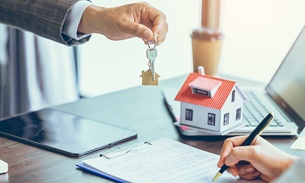 close person handing over the keys to a new home to another person signing mortgage documents at a table.