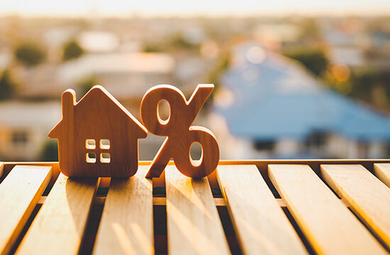 Wood house symbol next to percentage icon sitting on a wooden table. Symbolizing Mortgage Rates.