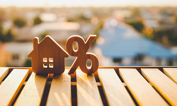 Wood house symbol next to percentage icon sitting on a wooden table. Symbolizing Mortgage Rates.