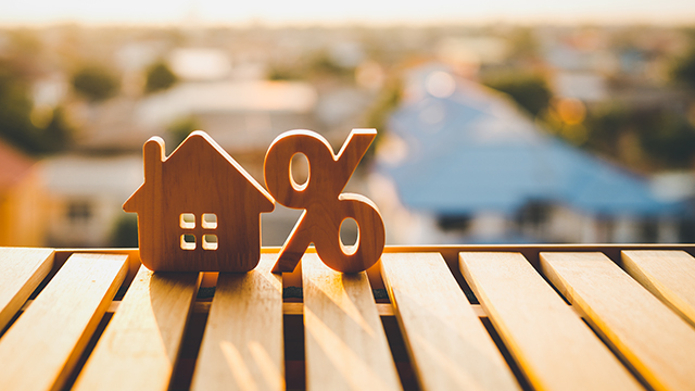 Wood house symbol next to percentage icon sitting on a wooden table. Symbolizing Mortgage Rates.