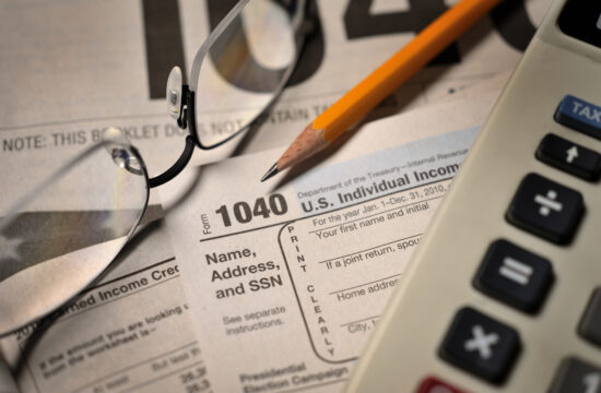 Glasses, pencil, and calculator sitting on top of a stack of 1040 IRS Tax forms