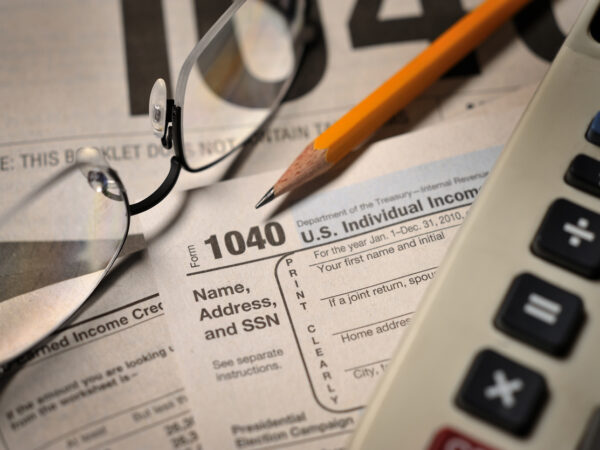 Glasses, pencil, and calculator sitting on top of a stack of 1040 IRS Tax forms