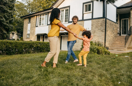 Parents playing with their child outside in front yard of house.