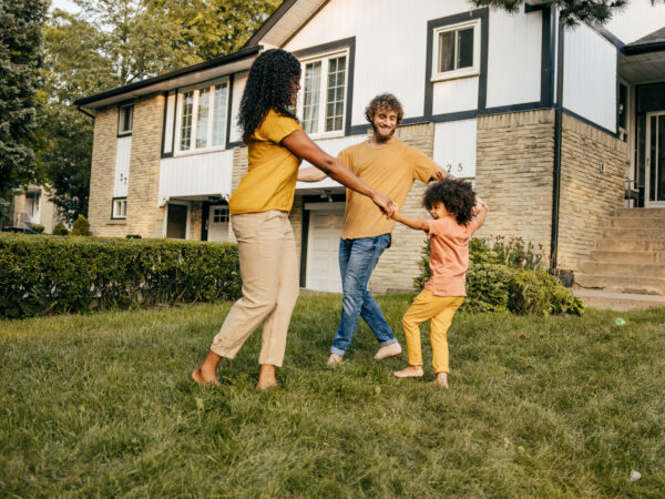 Parents playing with their child outside in front yard of house.