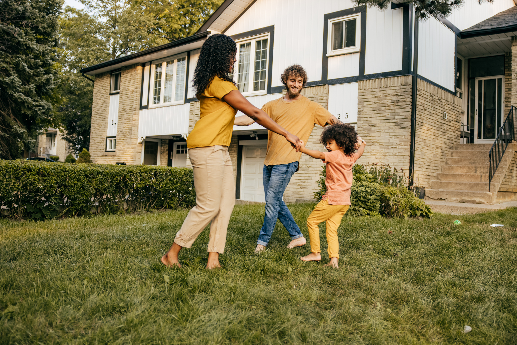 Parents playing with their child outside in front yard of house.