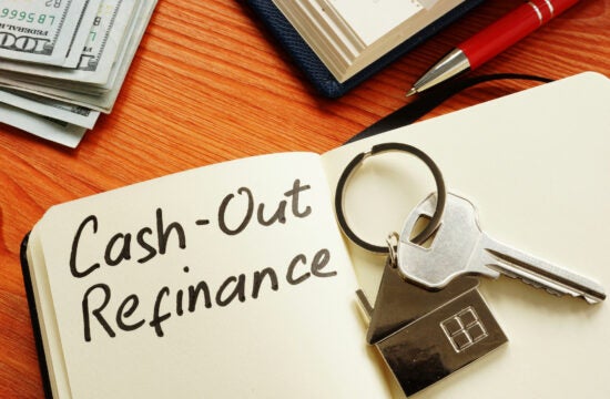 Notebook sitting on a wood table opened to a page that says Cash-Out refinance with a house key sitting on top.