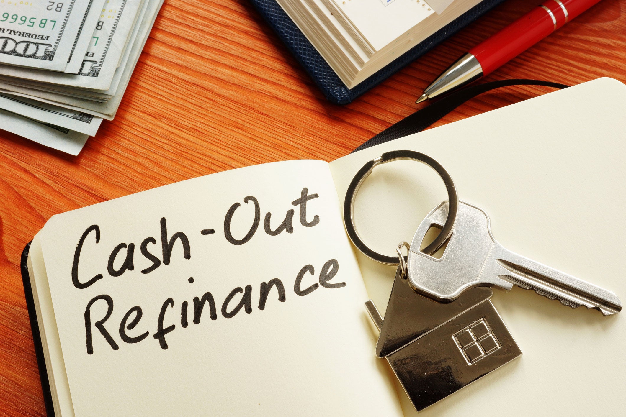 Notebook sitting on a wood table opened to a page that says Cash-Out refinance with a house key sitting on top.