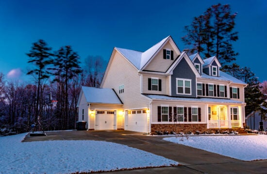 A two-story home at dusk with light snow covering the grass and the roof.
