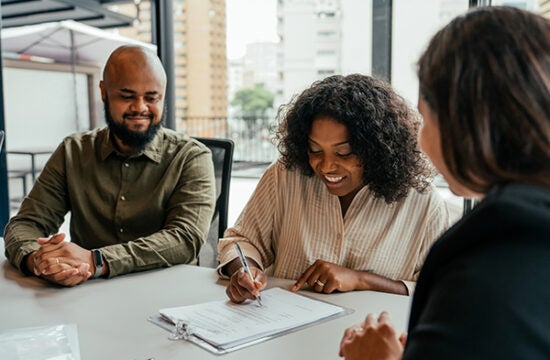 Husband and wife sitting at a table signing mortgage paperwork in attorney's office