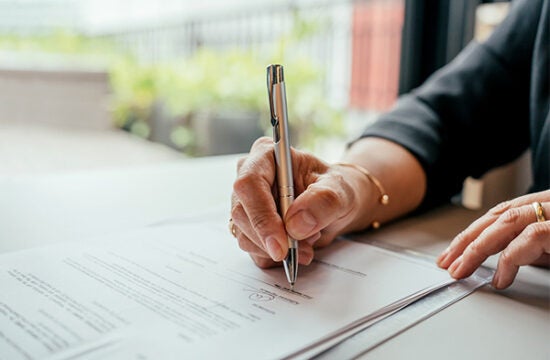 Close up of hand holding pen and signing mortgage documents.